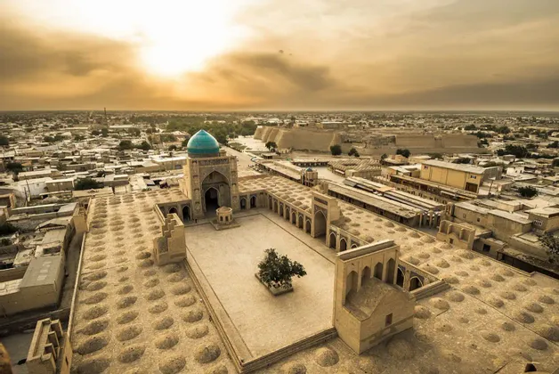 Una vista aerea di una città storica al tramonto, con una grande moschea dalla cupola turchese e un cortile centrale.