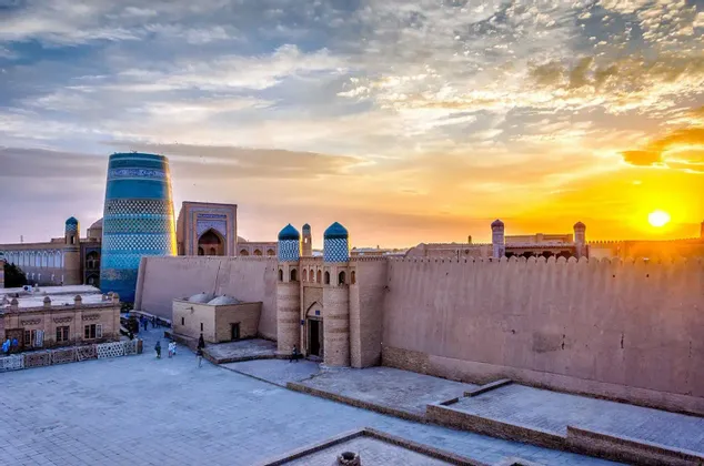 Una città antica con alte mura di fortezza e un grande minareto dalle piastrelle blu risplende durante un tramonto dorato.