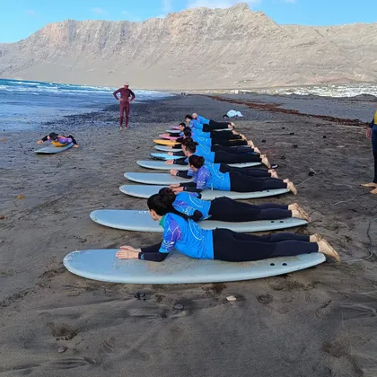 Un gruppo WeRoad segue una lezione di surf, esercitandosi sulle tavole su una spiaggia di sabbia nera sotto lo sguardo di un istruttore.
