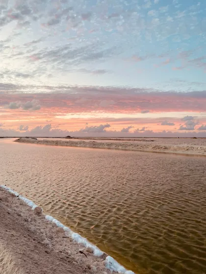 Salines avec des canaux d'eau reflétant un ciel de coucher de soleil coloré avec des nuages roses et bleus.