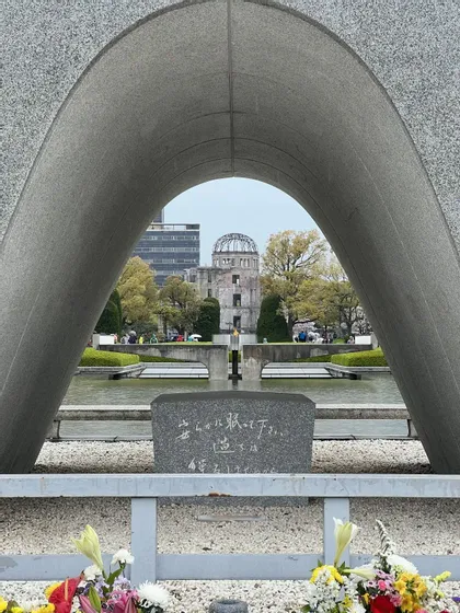 Vista attraverso un grande arco commemorativo in granito che incornicia una rovina a cupola e una fiamma su una vasca d'acqua in un parco.