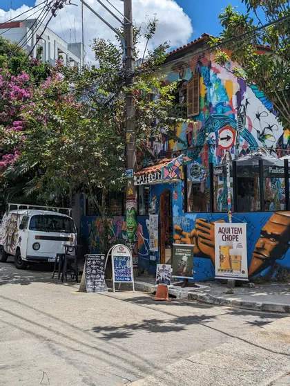 Un café-bar d'angle dans une rue de ville, ses murs couverts de peintures murales colorées et de graffitis, avec une fourgonnette blanche garée à proximité.