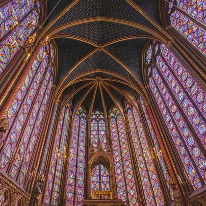 Una vista dal basso dell'interno di una cappella con imponenti e vivaci vetrate colorate e un soffitto a volta scuro decorato con stelle d'oro.
