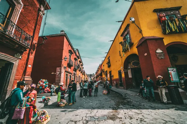 Un viaje en grupo de WeRoad en una concurrida calle empedrada entre edificios coloridos rojos y amarillos bajo un cielo brillante.