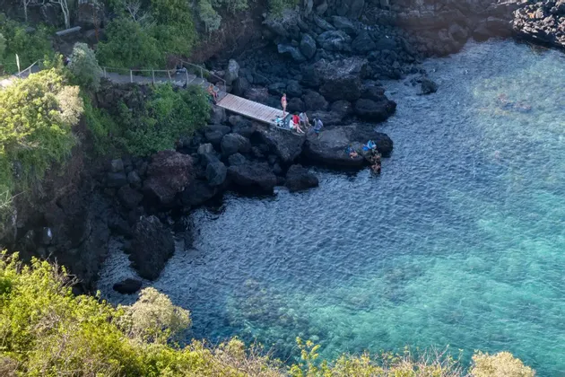 Vista aérea de un viaje en grupo de WeRoad relajándose en un muelle de madera y nadando en el mar azul transparente junto a una costa rocosa.