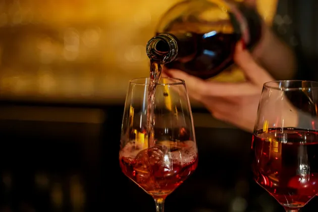 Primo piano di vino rosato versato da una bottiglia in un calice su uno sfondo caldo con effetto bokeh.