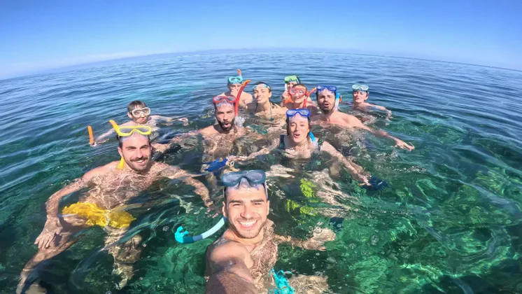 Un groupe WeRoad en voyage, équipé de masques et tubas, sourit pour un selfie en nageant dans une eau turquoise cristalline.