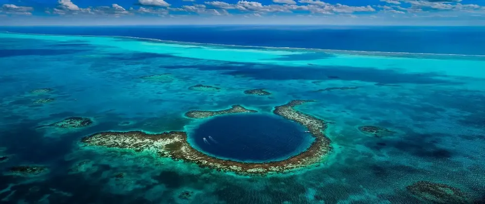 Una vista aerea di un grande buco blu circondato da una barriera corallina in acque turchesi, con due piccole imbarcazioni che vi navigano all'interno.