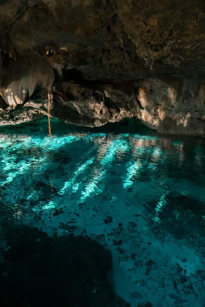 La luce del sole illumina l'acqua turchese increspata all'interno di una grotta di roccia buia, creando giochi di luce sulla superficie.