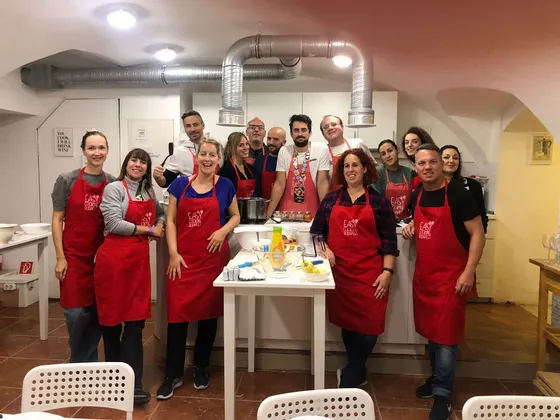 Un gruppo WeRoad sorride per una foto durante una lezione di cucina, tutti indossano grembiuli rossi coordinati in una cucina.