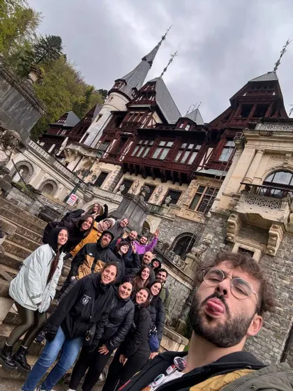 Un uomo si fa un selfie con un viaggio di gruppo WeRoad su scale di pietra, con un grande castello ornato sullo sfondo.