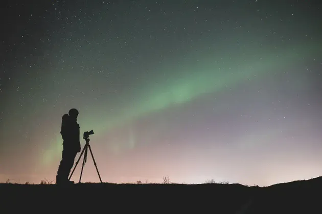 Silhouette di un fotografo con la macchina fotografica su treppiede che osserva l'aurora boreale sotto un cielo stellato