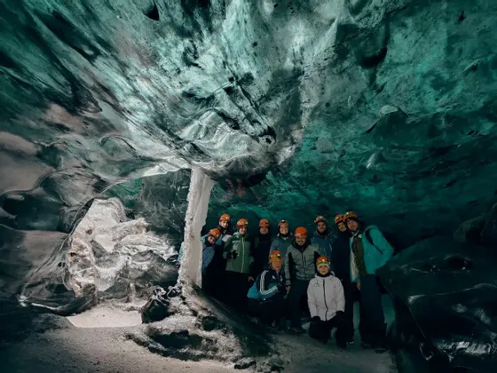 Un gruppo WeRoad con caschi e lampade frontali posa per una foto di gruppo all'interno di una grande grotta di ghiaccio con pareti turchesi.