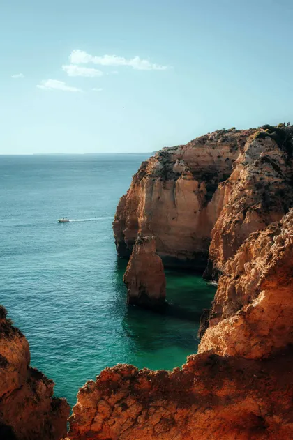 Una barca naviga su acqua turchese accanto a grandi scogliere arancioni sotto un cielo limpido.