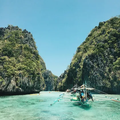 Un viaggio di gruppo WeRoad su una piroga naviga un canale di acqua turchese tra alte scogliere rocciose e verdi