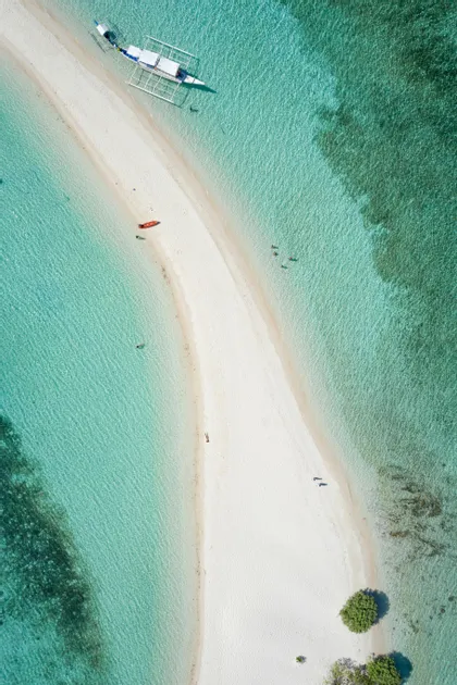 Veduta aerea di un banco di sabbia bianco in acqua turchese, con una barca e diverse persone che si rilassano sulla spiaggia.