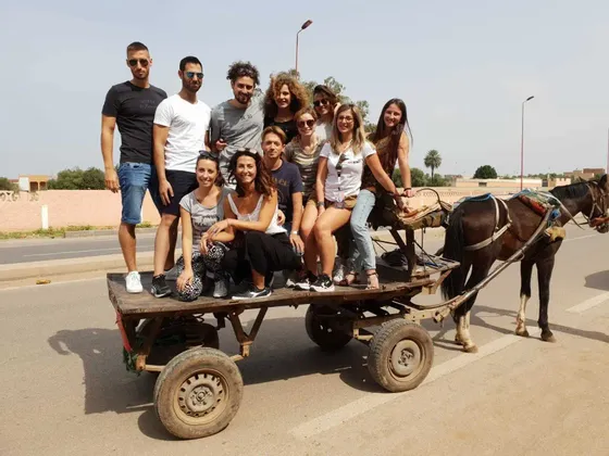Un voyage de groupe WeRoad posant pour une photo sur une charrette rustique tirée par des chevaux, garée sur le côté d'une route pavée.