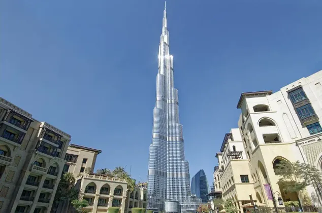 Un moderno grattacielo di vetro si erge su edifici in stile tradizionale sotto un cielo azzurro brillante.