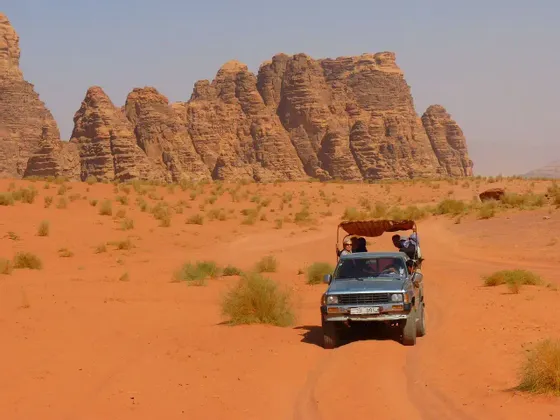 Un viaggio di gruppo WeRoad a bordo di un camion scoperto che attraversa un deserto di sabbia rossa con grandi formazioni rocciose sullo sfondo.