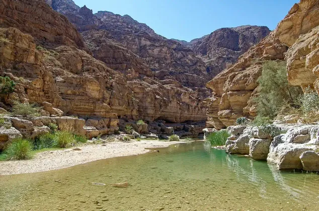 Un fiume poco profondo con acqua verde chiara scorre attraverso un ripido canyon roccioso in una giornata di sole