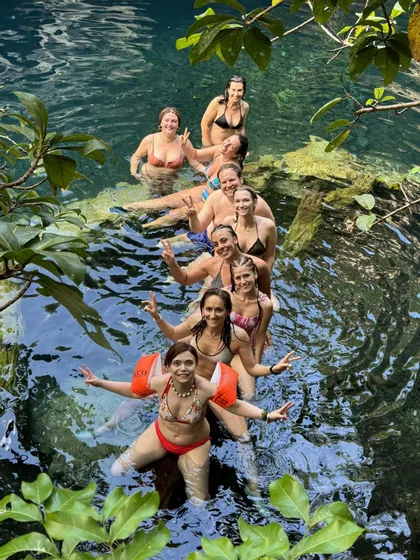 Un viaje en grupo WeRoad posando en fila sobre un tronco sumergido en agua turquesa cristalina, rodeados de follaje selvático.