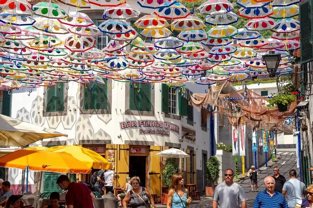 Un baldacchino di ombrelli colorati a pois pende su una stretta via piena di persone e caffè all'aperto.