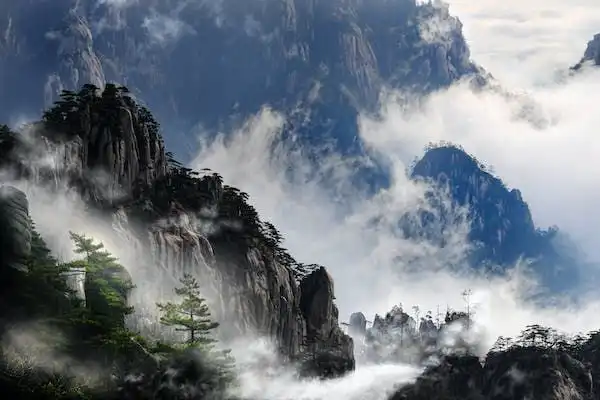 Vette rocciose coperte di pini emergono da uno spesso strato di nebbia e nuvole.