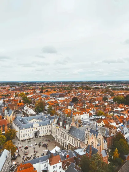 Vista aerea di una storica città europea con fitti tetti rossi e una piazza centrale sotto un cielo nuvoloso.