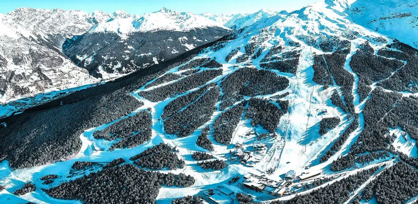 Una vista aerea di una grande stazione sciistica con numerose piste scavate in una foresta coperta di neve su una montagna.