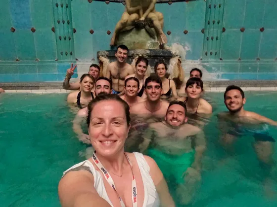 Eine WeRoad-Gruppe entspannt sich in einem Innen-Thermalbad mit Zierbrunnen und macht dabei ein Selfie.