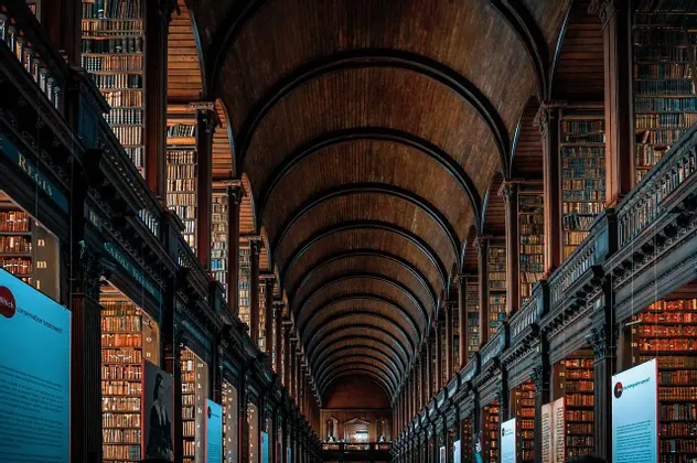 Il lungo salone di una biblioteca storica con un soffitto alto, ad arco in legno e pareti rivestite di imponenti librerie.