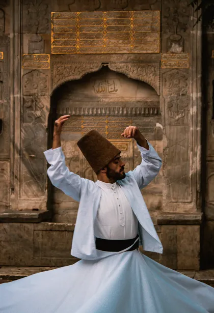 Un hombre con túnicas blancas tradicionales y un sombrero alto marrón realiza una danza giratoria frente a un muro de piedra ornamentado y tallado.