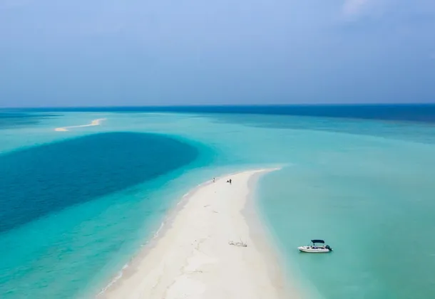 Veduta aerea di un viaggio di gruppo WeRoad su un banco di sabbia bianca circondato da acqua turchese, con una piccola barca ancorata nelle vicinanze.