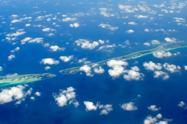 Vista aerea di una lunga catena di atolli tropicali in un oceano blu intenso, punteggiata da piccole nuvole bianche.