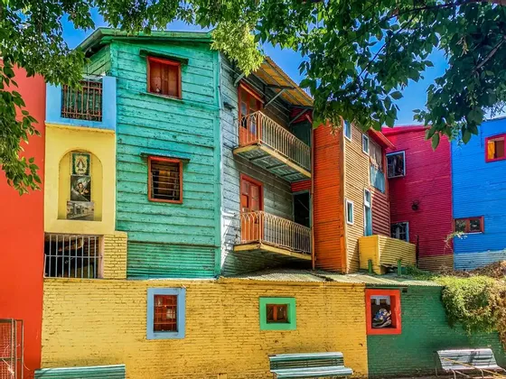 Vue extérieure de bâtiments colorés empilés, peints en turquoise, jaune, rouge et bleu sous des feuilles d'arbres verts et un ciel clair.