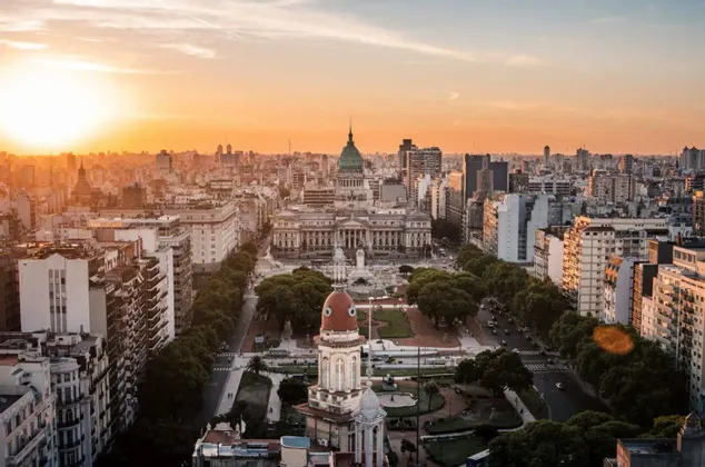 Vue aérienne d'un paysage urbain dense centré sur un grand bâtiment avec un dôme vert et une place au coucher du soleil.