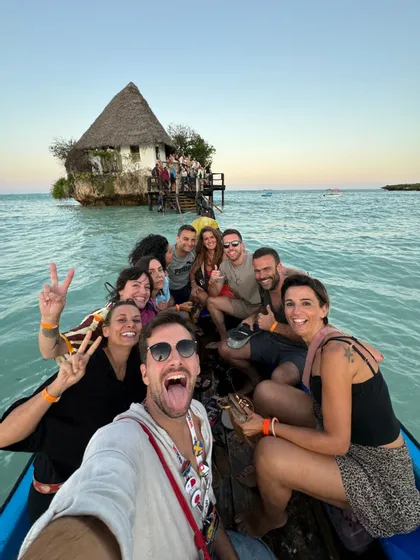 Un grupo de WeRoad se hace un selfie en un barco con un edificio sobre una roca de fondo.