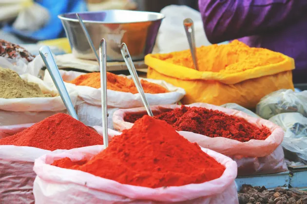 Vivaci spezie macinate rosse, arancioni e gialle sono esposte in grandi sacchi aperti con palette di metallo in un mercato.