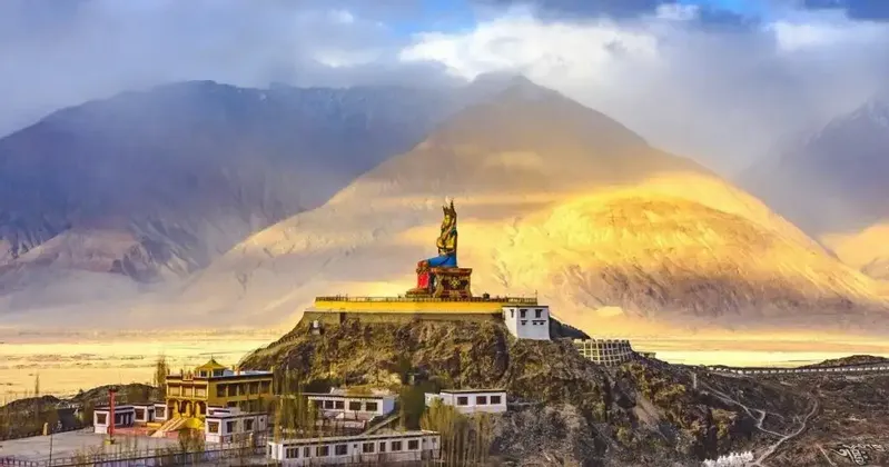 Una grande statua del Buddha seduto su un monastero in cima a una collina si affaccia su una valle con vaste montagne sullo sfondo