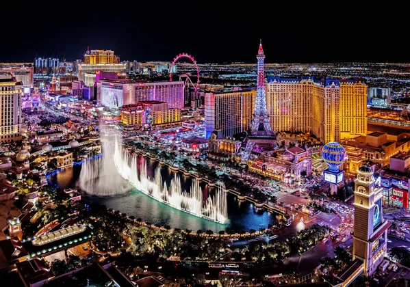 Veduta aerea di uno skyline cittadino di notte, con edifici illuminati, un grande spettacolo di fontane e una replica della Torre Eiffel.