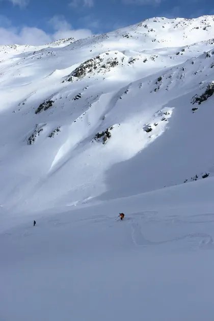 Due persone sciano su un'ampia pista di montagna innevata, lasciando nuove tracce nella neve fresca.