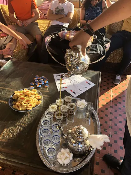 Une personne verse du thé d'une théière en argent ouvragée dans de petits verres pour un groupe WeRoad attablé.