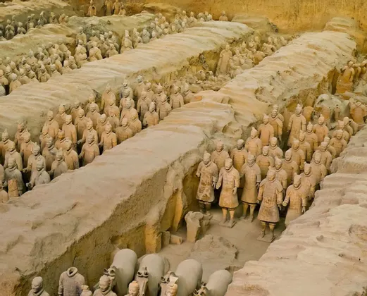 Reihen lebensgroßer Terrakotta-Krieger-Statuen stehen in Formation in großen, ausgehobenen Erdgruben.