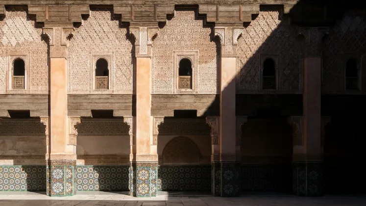 La facciata dettagliata di un edificio con muri scolpiti, piastrelle colorate e finestre ad arco, sotto una forte luce e ombra.