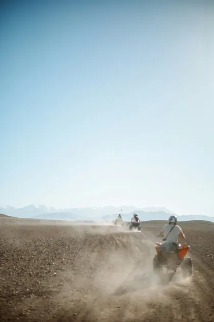 Un viaggio di gruppo WeRoad in quad su un sentiero polveroso nel deserto, con le montagne visibili in lontananza.