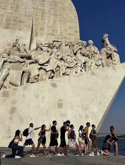 Un gruppo WeRoad in viaggio in posa in fila per imitare le statue su un grande monumento vicino all'acqua.