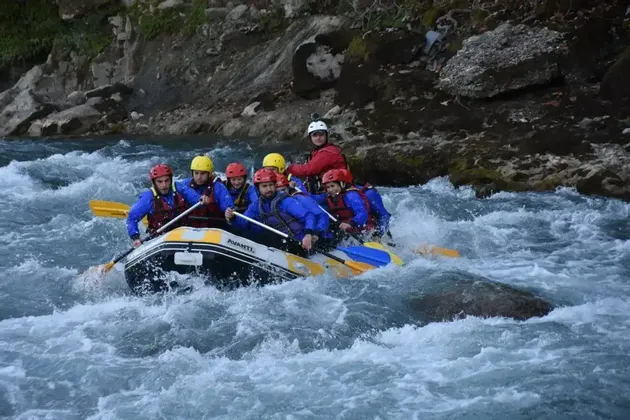 Eine WeRoad Gruppenreise in Helmen und Schwimmwesten navigiert ein Schlauchboot durch turbulentes Wildwasser.