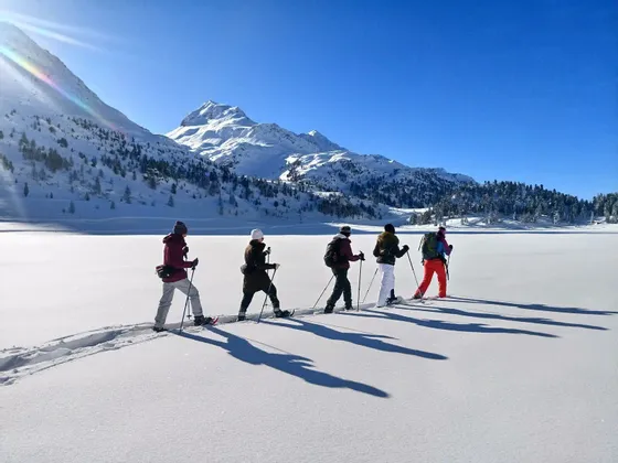 Un viaggio di gruppo WeRoad con persone che camminano con le ciaspole in fila attraverso un paesaggio innevato con montagne sullo sfondo.