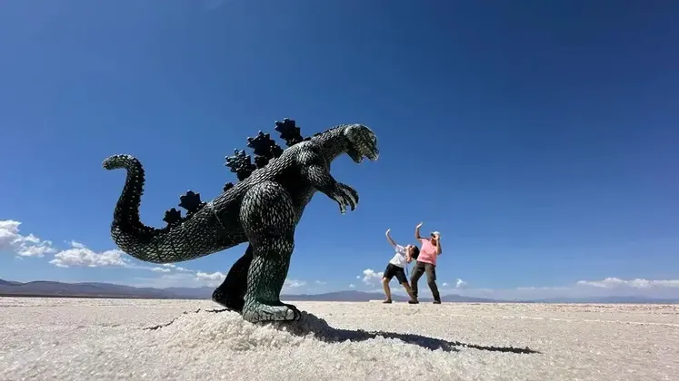 Un viaggio di gruppo WeRoad usa la prospettiva forzata con un giocattolo di Godzilla su una distesa salata, con due persone che fingono di essere spaventate.