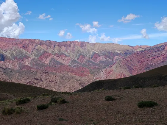 Una catena montuosa con strati a strisce colorate di rosso, viola e beige sotto un cielo blu parzialmente nuvoloso.